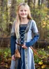 A young girl in a medieval-style dress stands in a forest setting. Produktbild-Vorschau