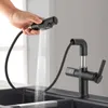 A hand is holding a black pull-down kitchen faucet spray head, with water spraying out into a sink. The faucet base is also visible, with a digital display showing the temperature. Podgląd zdjęcia produktu