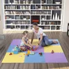A woman and a child are playing with building blocks on a colorful puzzle mat in front of a large bookshelf. Voir les images du produit