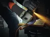 A person is using an angle grinder to cut a metal pipe, with sparks flying. Produktbild-Vorschau