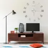 A living room scene featuring a large wall clock, a TV stand with a TV, a floor lamp, and decorative items. Voir les images du produit