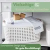 A white laundry basket filled with folded towels and two small wooden cubes, placed on a shelf. Produktbild-Vorschau