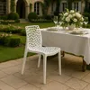 A white chair is placed on a patio in front of a table set for a meal, with a garden and house in the background. Produktbild-Vorschau