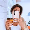 A woman takes a selfie while holding a coffee cup and a clear phone case. Produktbild-Vorschau