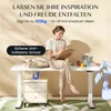 A woman is sitting on a white desk, writing on a clipboard, with a cat sleeping on the desk. There are art supplies on the desk. Produktbild-Vorschau