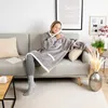 A woman is sitting on a couch wearing a gray sherpa hoodie blanket. Produktbild-Vorschau