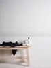 A wooden bench with a dark towel and some bathroom products on it, placed against a wall with a decorative border. Náhled obrázku produktu
