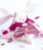 A plush toy rabbit with long ears and a pink blanket draped over it, set against a white background with scattered pink and purple confetti. Podgląd zdjęcia produktu