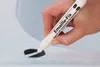 A hand is using a white marker pen labeled 'Emaille-Fix' to repair a scratch on a white surface. Produktbild-Vorschau