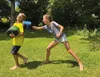 Two children are playing outside in the grass, one is punching the other with boxing gloves. Produktbild-Vorschau