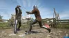 Two knights in armor are engaged in a sword fight in an outdoor training area with tents and a wooden fence in the background. Produktbild-Vorschau