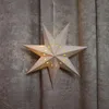 A paper star lantern with cut-out star shapes and small dots, illuminated from within, hangs in front of a textured gray curtain. Voir les images du produit