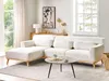 A modern living room scene featuring a white bouclé sectional sofa with a chaise lounge, a round coffee table with a cup of coffee, and decorative items on a wooden credenza. Podgląd zdjęcia produktu