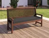 A wooden bench with a black cushion is placed on a wooden deck outdoors, with grass and a building in the background. Produktbild-Vorschau