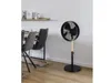 A black and wood-tone stand fan is positioned in a dining area next to a table and chairs. Voir les images du produit