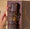 A close-up shot of a person's finger pressing a power button on a miniature model of Diagon Alley from Harry Potter. The model is detailed with brickwork and illuminated windows. Produktbild-Vorschau