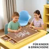 Two children are assembling a jigsaw puzzle on a table with a puzzle board that has drawers. Produktbild-Vorschau