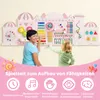 A woman and a child are interacting with a large, pink, wooden activity wall designed for toddlers. The wall is mounted on a light-colored wall and features various interactive elements like gears, a xylophone, beads, and a clock. The bottom of the image h Produktbild-Vorschau