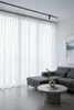 A modern living room with sheer white curtains, a grey sectional sofa, and a concrete coffee table with a vase and plant. Produktbild-Vorschau