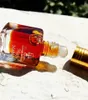 A close-up shot of a small glass perfume bottle with a rollerball applicator and a gold cap, lying on its side on a textured surface. Voir les images du produit