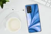 A smartphone with a blue abstract design case, placed on a white desk next to a cup of coffee and earphones. Produktbild-Vorschau