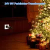 A Christmas tree decorated with lights and ornaments, with gifts underneath. A power adapter is plugged into a wall socket. Produktbild-Vorschau