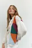 A woman is posing in a studio setting, wearing a colorful knitted cardigan. Produktbild-Vorschau