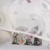A close-up view of a white sheer curtain with a floral burnout pattern, partially covering a floral image and a roll of fabric. Produktbild-Vorschau