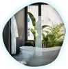 A modern bathroom with a freestanding bathtub, bidet, and plants, reflected in an irregular mirror. Produktbild-Vorschau