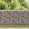 A gabion wall filled with stones, with grass and a paved area in front, and trees in the background. Náhľad obrázku produktu