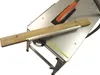 A close-up view of a table saw with a piece of wood positioned on it. Náhled obrázku produktu