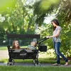 A woman pushing a wagon with two children in it, outdoors in a park-like setting. Náhled obrázku produktu