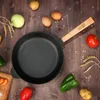 A cast iron pan is placed on a wooden table surrounded by ingredients like potatoes, onions, eggs, tomatoes, and bell peppers, along with wheat stalks and scattered grains. Produktbild-Vorschau