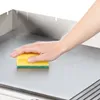 A hand is cleaning a flat metal surface with a yellow and green sponge. Náhled obrázku produktu