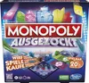 The image shows the front of a Monopoly Ausgezockt board game box, featuring colorful graphics of buildings and game elements. Produktbild-Vorschau