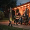 People gathered around a patio heater on a patio at dusk, with one person playing a guitar and a dog present. Náhľad obrázku produktu