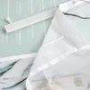 A close-up view of a white sheer curtain with a velcro strip and a small white plastic fastener, placed on a light green background with text. Produktbild-Vorschau