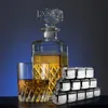 A decanter and glass filled with whiskey, alongside a stack of stainless steel whiskey stones, set against a gradient blue background. Produktbild-Vorschau