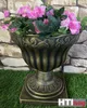 A decorative planter with pink flowers on a grassy surface in front of a stone wall. Produktbild-Vorschau