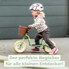 A young child rides a green balance bike with a basket on the front. Produktbild-Vorschau