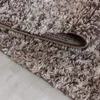 A close-up view of a beige, high-pile rug with a marbled pattern, folded over to reveal its backing. Produktbild-Vorschau