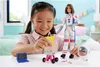 A young girl is playing with a Barbie astronaut doll and accessories in a bedroom setting. Produktbild-Vorschau