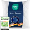 A white quilted pillow with a dark blue label featuring product information and certifications. Produktbild-Vorschau