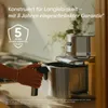 A person's hand is shown operating a silver and black air fryer in a kitchen setting. Produktbild-Vorschau
