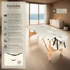 A white massage table set up in a room with a large window overlooking the ocean. The table has accessories like a headrest and armrests. A side panel lists product features. Náhled obrázku produktu