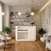 A reception desk in a clean, modern salon or spa setting, with shelves of products in the background and seating areas. Produktbild-Vorschau