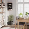 A corner shelf unit filled with books and decorative items, placed next to a window with a dining table and chairs in the foreground. Voir les images du produit