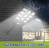 A solar-powered LED street light is shown mounted on a dark, textured wall, with a second street light visible in the background. The scene depicts a stormy night with lightning and rain, suggesting the product's durability. Houses are visible in the backg Voir les images du produit