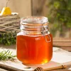 A jar of honey with a honey dipper and rosemary on a wooden surface. Anteprima dell’immagine prodotto