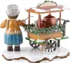 A wooden figurine of a person standing next to a cart selling hot drinks, decorated with snow and pine branches. Produktbild-Vorschau